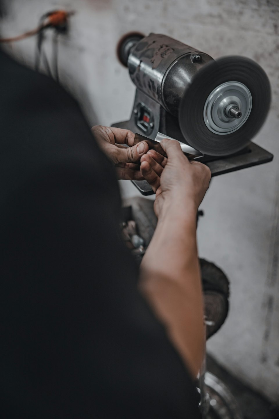 Hands polish a metal object on a spinning buffing wheel.